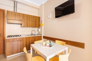 Una cucina compatta con mobili in legno, un fornello a gas, un lavello e un'area pranzo con un tavolo bianco e sedie gialle.