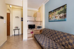 Un soggiorno con un divano a fantasia, una televisione, un forno a microonde e un quadro appeso al muro.