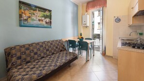 A living area with a sofa, a dining table with chairs, a kitchen with a stove, and a painting on the wall. - Holiday Apartment Isophylla Standard with Balcony & Wi-Fi (Finale Ligure)