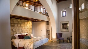 Un dormitorio con pared de piedra, una cama con estructura metálica, una silla y una mesita.