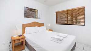 Ein ordentlich eingerichtetes Schlafzimmer mit Bett, Nachttischen, Deckenventilator, Wandkunst und einem Fenster mit Jalousien.