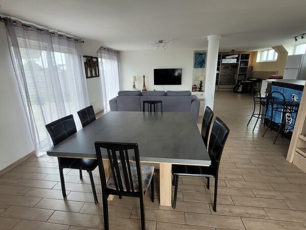 Un comedor con una mesa grande y sillas, un sofá y un televisor montado en la pared.