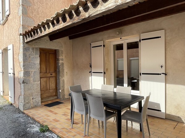 A patio with a table and chairs, a wooden door, and a white-framed window.