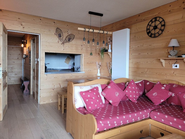 L’intérieur chaleureux d’un chalet en bois, avec un canapé en bois, un coin cuisine et une horloge murale décorative.