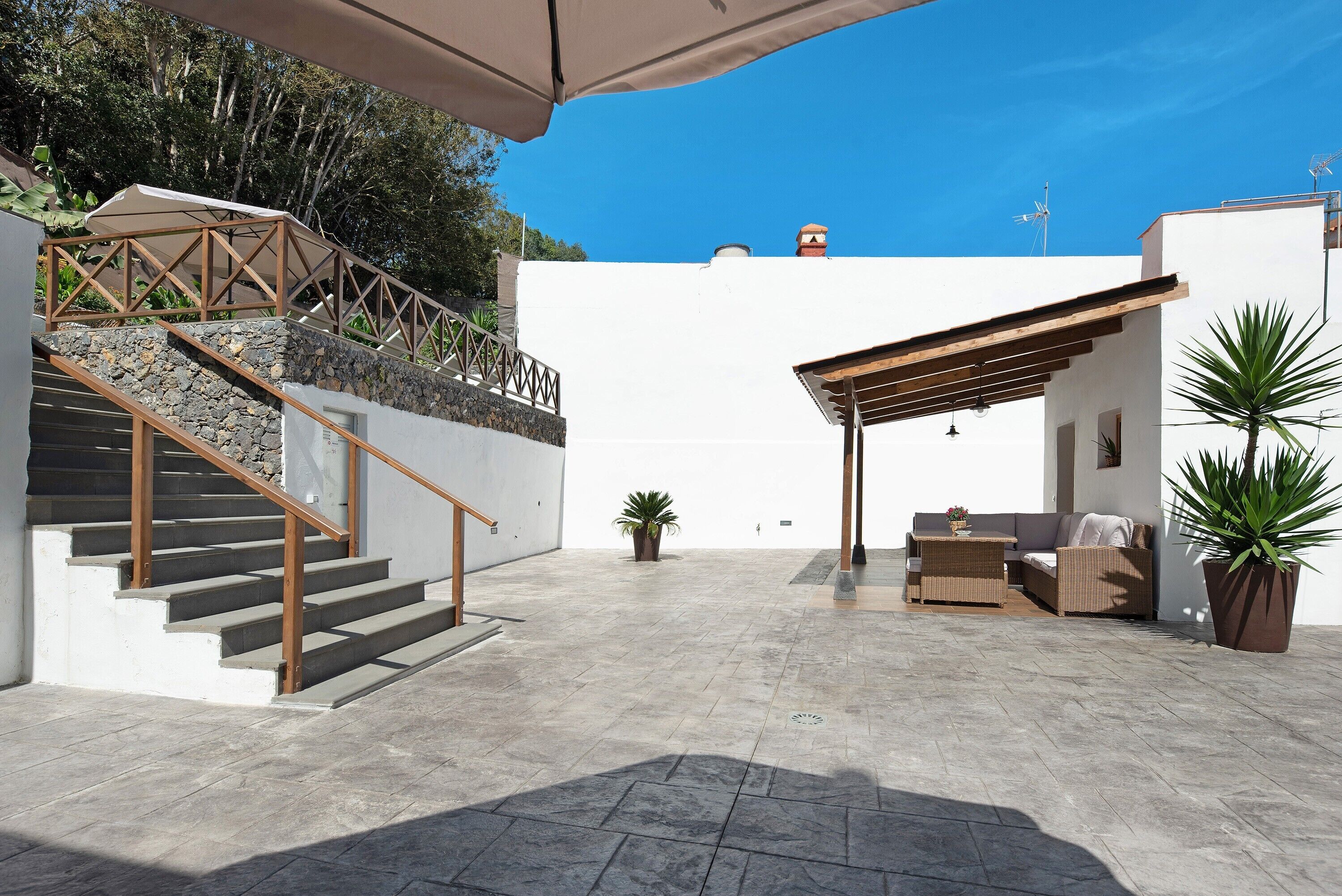 A covered outdoor area with a staircase, a seating area, and potted plants.