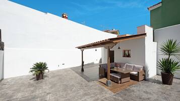 A patio with a wooden table and chairs, potted plants, and a white wall.