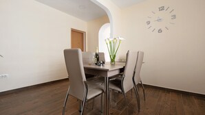 Un coin repas comprenant une table en bois, quatre chaises, une horloge murale et un vase avec des fleurs.