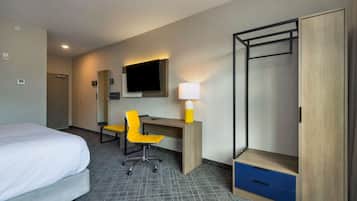 Habitación de hotel con cama, escritorio con silla, lámpara, armario y televisor en la pared.