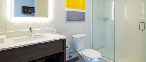 Un baño moderno con cabina de ducha de vidrio, un lavamanos blanco y un inodoro.