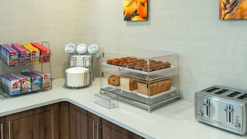 A breakfast bar with cereal boxes, a coffee maker, a toaster, and a display of muffins and bread.