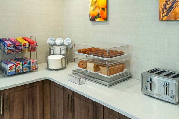 A breakfast bar with cereal boxes, a coffee maker, a toaster, and a display of muffins and bread.