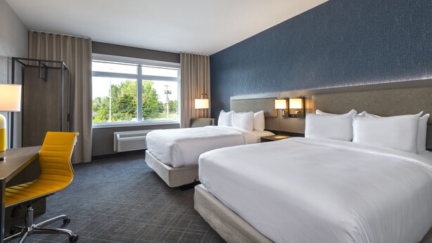 A hotel room with two beds, a desk, a chair, and a large window with curtains.