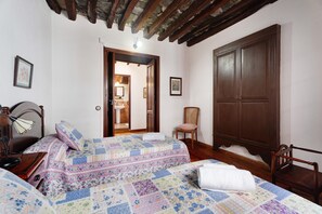 A bedroom with two beds, wooden furniture, a wardrobe, and a door leading to a bathroom.