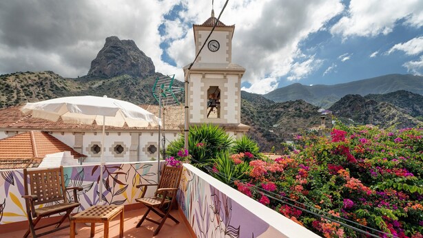 A terrace with a view of mountains, a clock tower, and colorful flowers. - Historic 'Casa de Telégrafos' with Mountain Views, Private Terrace & Wi-Fi (vallehermoso)
