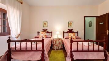 Una habitación con dos camas de madera, un tapete verde, una mesita redonda con una lámpara y una puerta.