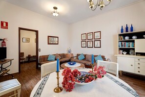 A living room with a sofa, a dining table with a vase, a bookshelf, and a fireplace.