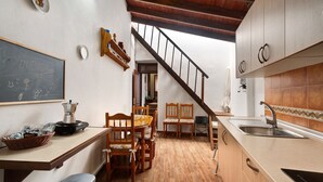 A kitchen with wooden cabinets, a chalkboard, a coffee machine, and a dining area with chairs. - Historic 'Casa de Telégrafos' with Mountain Views, Private Terrace & Wi-Fi (vallehermoso)