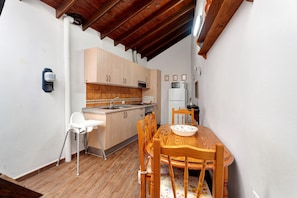A compact kitchen with wooden cabinets, a white countertop, a sink, and a dining area with a wooden table and chairs.