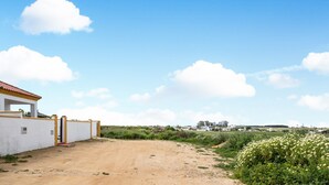 Ländliche Landschaft mit einem Feldweg, einem weißen Gebäude mit gelben Akzenten und einem strahlend blauen Himmel.