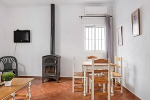 Une pièce avec une table en bois, des chaises, un téléviseur noir, une cheminée et une fenêtre avec des rideaux.