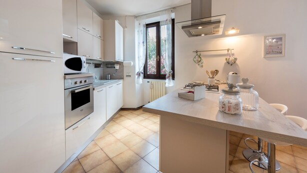 Una cocina moderna con armarios blancos, horno empotrado, microondas e isla grande con fregadero.