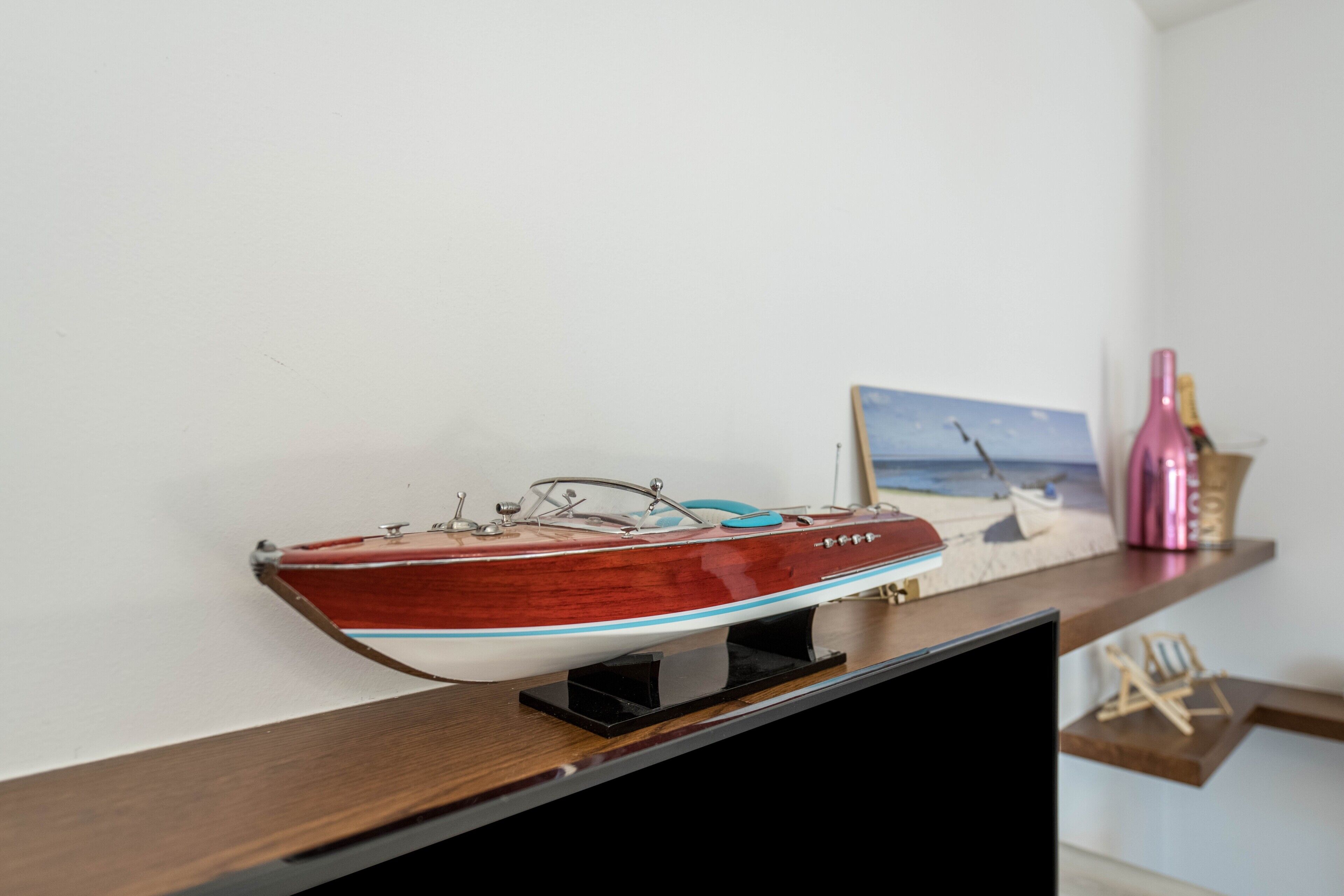 A model boat on a shelf, a framed picture, and a pink bottle.