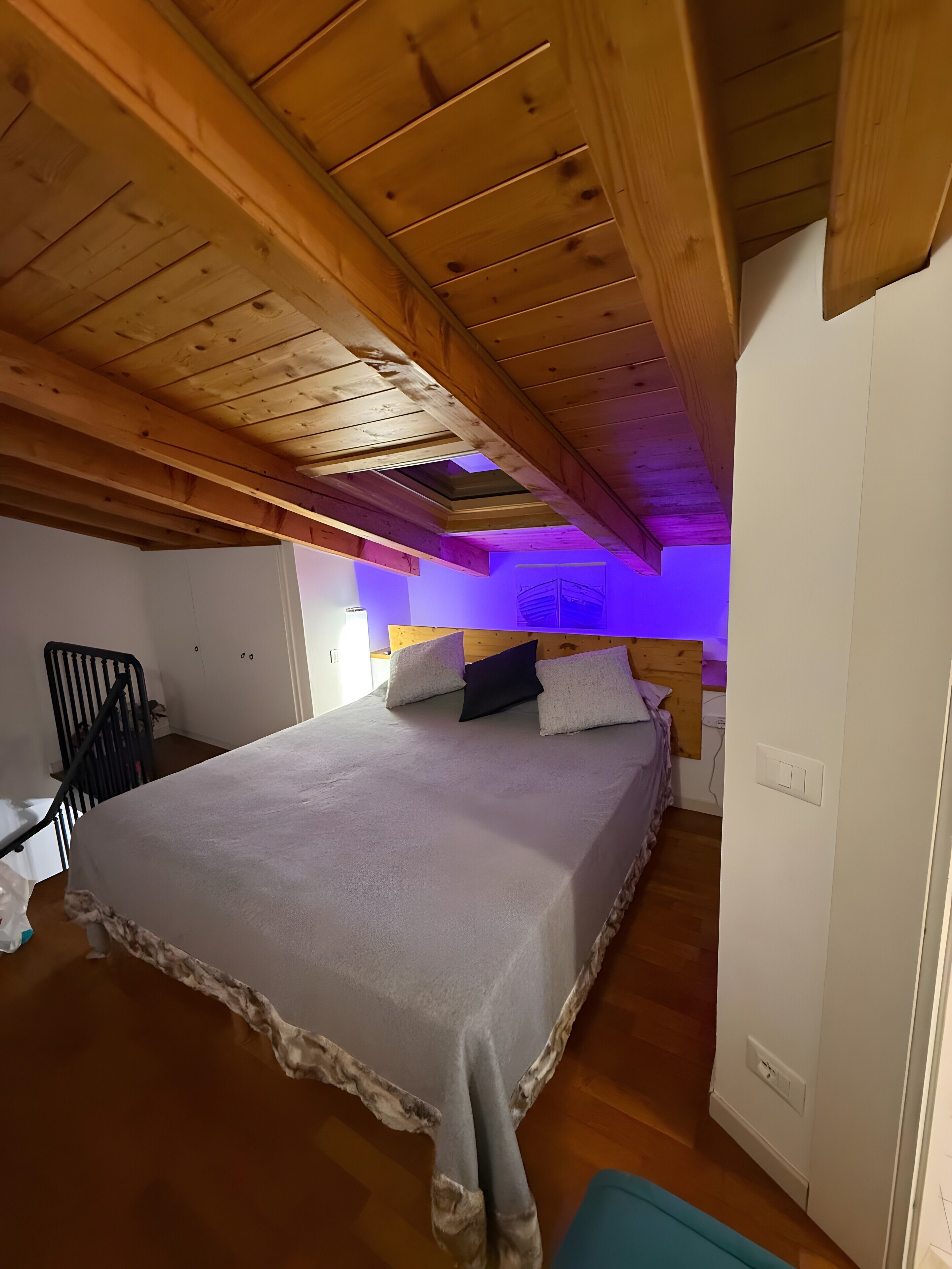 A bedroom with a wooden ceiling, a bed with a white mattress and pillows, a chair, and a small table.