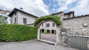 Un edificio de piedra con un porche cubierto, un camino de entrada con puerta de hierro y un seto.