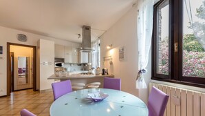 Una cocina moderna con armarios blancos, una mesa de comedor con sillas moradas y un ventanal con vistas a flores rosadas.