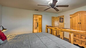 Une chambre à coucher comprenant un lit, un ventilateur de plafond, une commode en bois et une porte donnant sur une salle de bain.