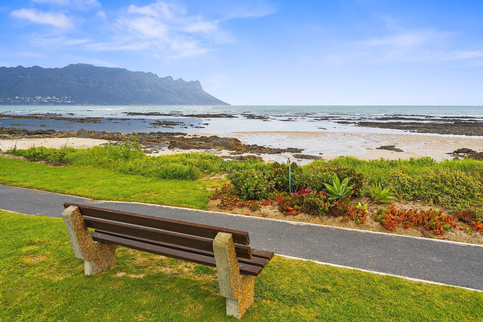 Un banc installé sur une pelouse, avec un sentier qui mène à une plage rocheuse et à l’océan.