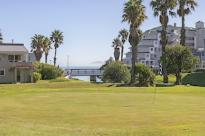 A golf course with a bridge, palm trees, and buildings in the background.