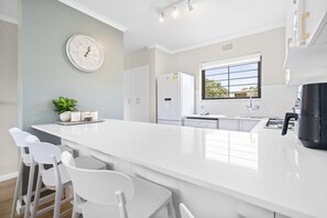 A modern kitchen with a central island, white bar stools, a refrigerator, and a window with a view. - Laguna Beach B8 (Cape Town)