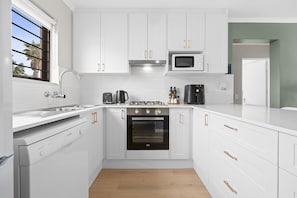 Une cuisine moderne avec des meubles blancs, des appareils en acier inoxydable et une fenêtre donnant sur des palmiers.