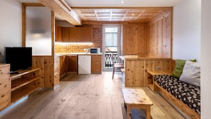 A compact room with a kitchenette, a bed, a TV, and a wooden floor.