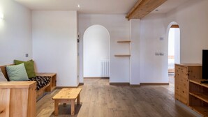 A spacious room with a wooden bench, a small table, and a sofa with patterned cushions. There are wooden shelves and a cabinet.