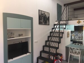 A staircase with black railings leading to a kitchen area with a tiled backsplash and a dining table with chairs.