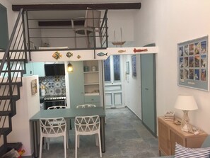 En kompakt opholdsstue med tekøkken, spiseplads og trappe op til en etage.