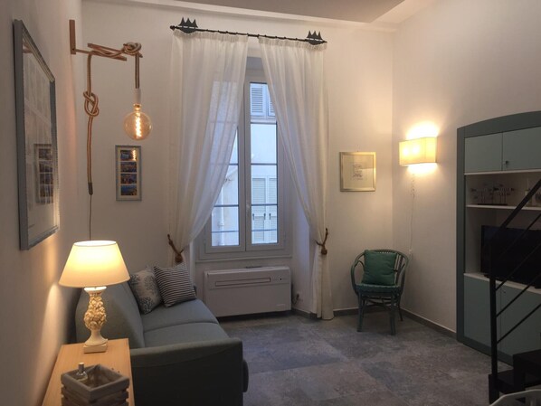 En hyggelig stue med sofa, lampe, stol, radiator og et vindue med gardiner.