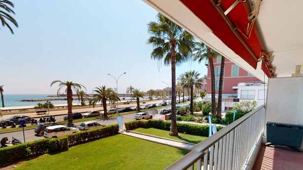 A balcony with a view of a well-maintained lawn, parked cars, and palm trees. - Spacious Studio with Sea View, Terrace, Near Center and Beaches in Menton (Menton)