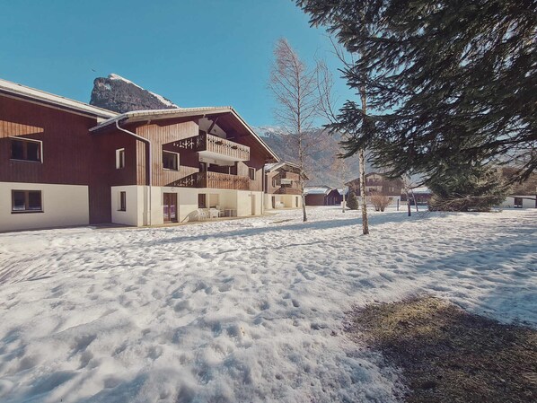 A modern building with a wooden facade and a balcony, surrounded by snow-covered ground and trees. - Family apartment with pools in Samoëns (Samoëns)