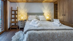 Un dormitorio con techo de madera, una cama con ropa de cama blanca, dos lámparas de noche, una escalera de madera y un armario.