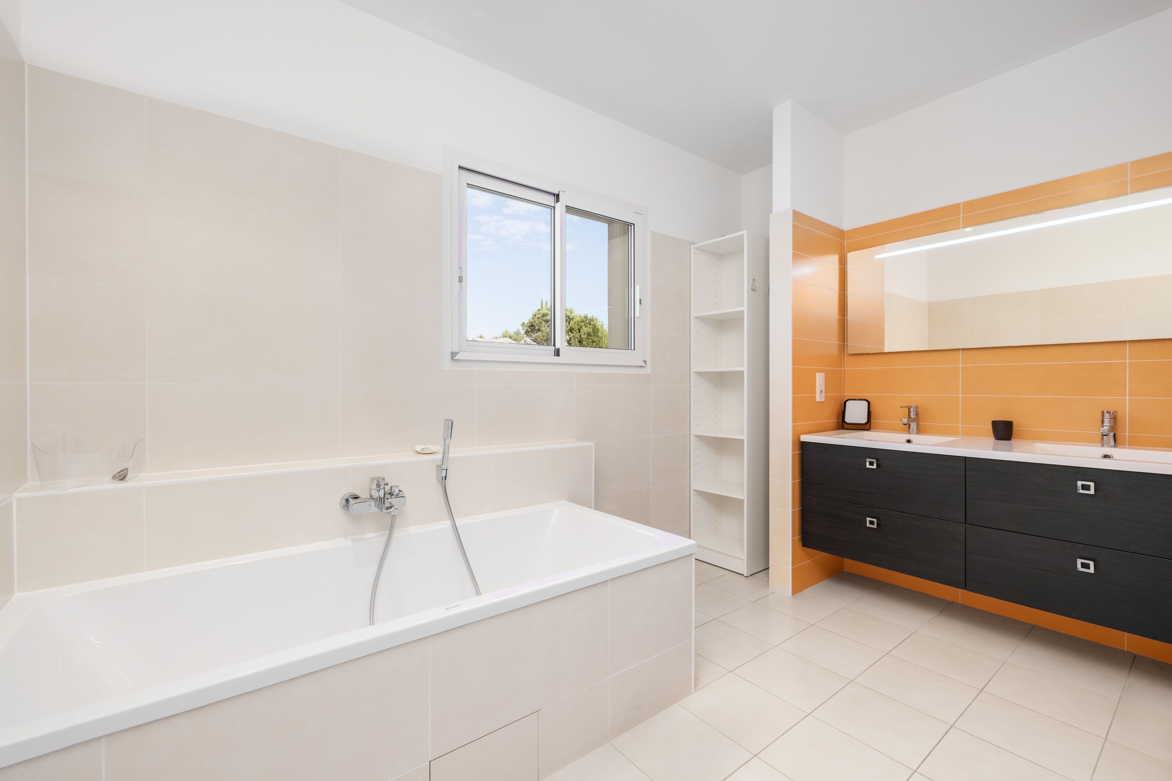 Een moderne badkamer met een badkuip, een raam en een wastafelmeubel met spiegel.