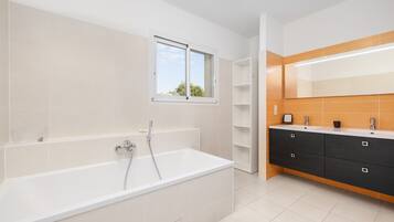 Een moderne badkamer met een badkuip, een raam en een wastafelmeubel met spiegel.