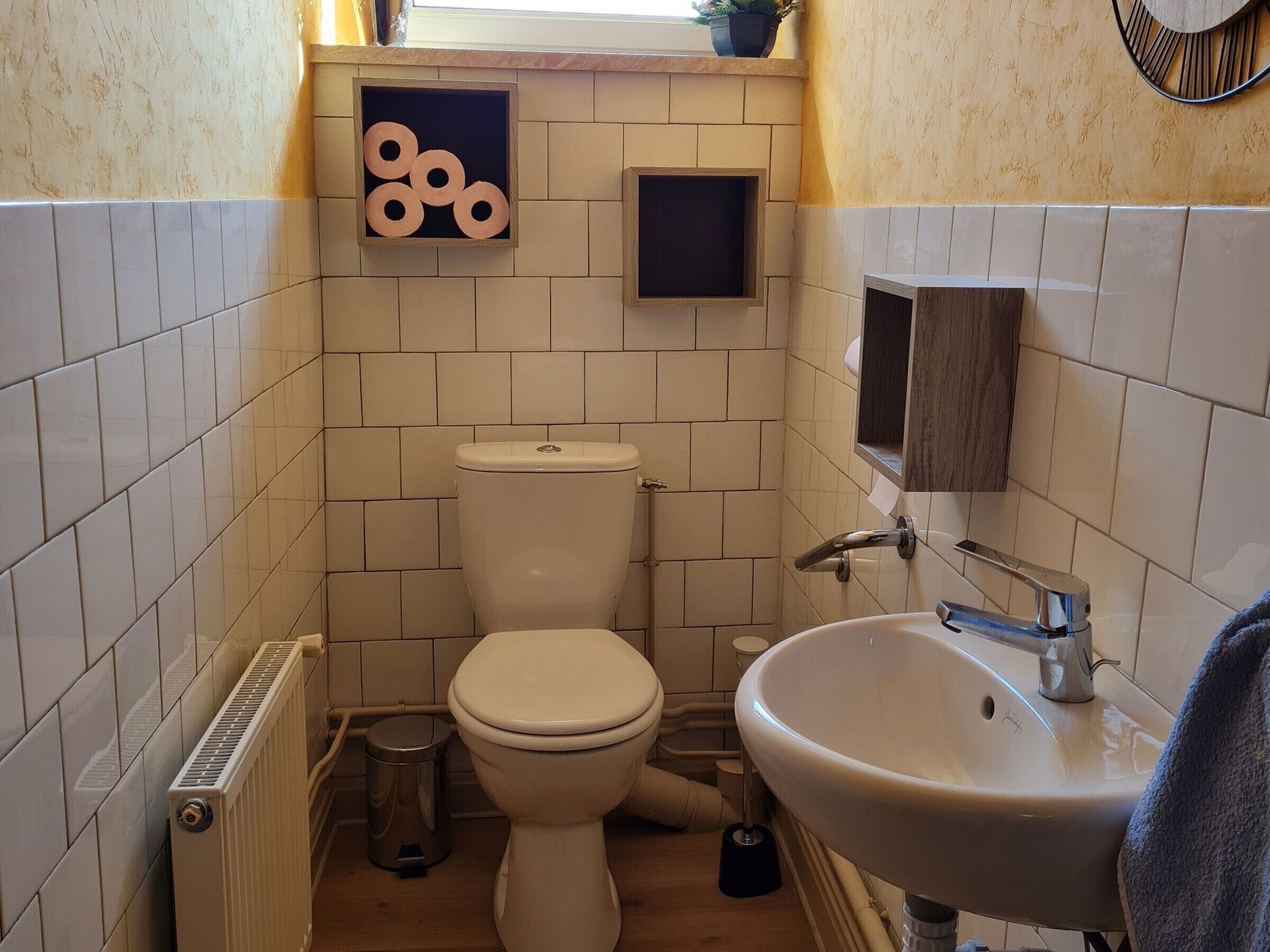 Ett litet badrum med toalett, handfat och en liten hylla med dekorativa föremål.
