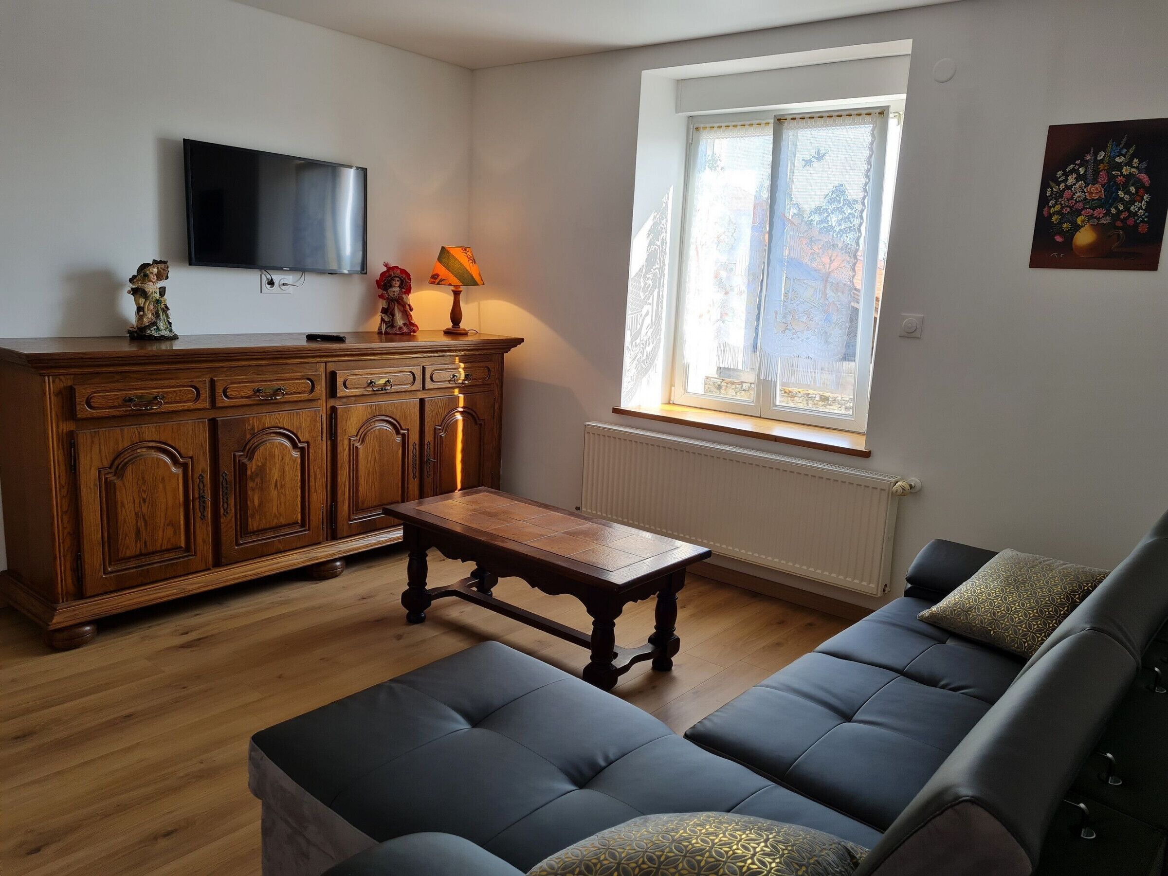 Un salon avec un meuble en bois, un téléviseur fixé au mur, un canapé et une fenêtre donnant sur l’extérieur.