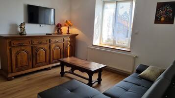 Un salon avec un meuble en bois, un téléviseur fixé au mur, un canapé et une fenêtre donnant sur l’extérieur.