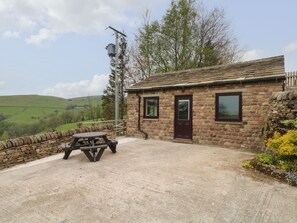 A stone cottage with a wooden door, a window, and a picnic table on a gravel path.
