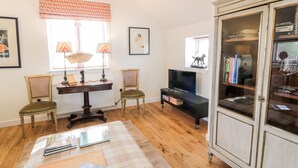 A living room with a wooden floor, a black TV stand, a glass cabinet, and a window with curtains.