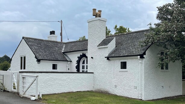 A white building with a black roof, a white fence, and a grassy yard.